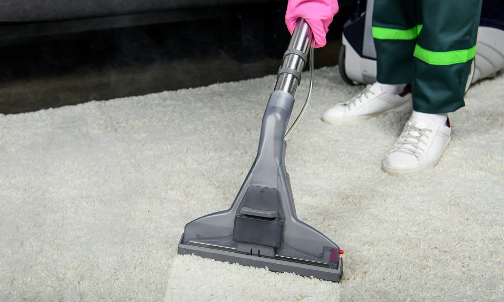 cropped shot of person in rubber glove cleaning carpet with vacuum cleaner