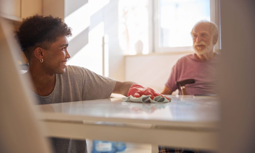 Smiling African American man in a rubber glove dusting the table with a mircofiber cloth